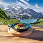 Gericht auf Holztisch mit Alpenlandschaft im Hintergrund