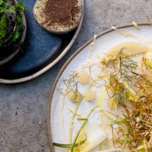 Stilvoll angerichtete Speise des Restaurant Rüpel aus Linden-Nord: Teller mit frischen Kräutern und Gemüse, daneben eine Schale mit grünem Salat und ein cremiger Dip auf handgefertigter Keramik