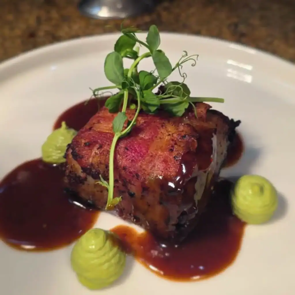 Zart geschmorte Ochsenbacke mit aromatischer dunkler Sauce und frischen Kräutern als Garnitur.