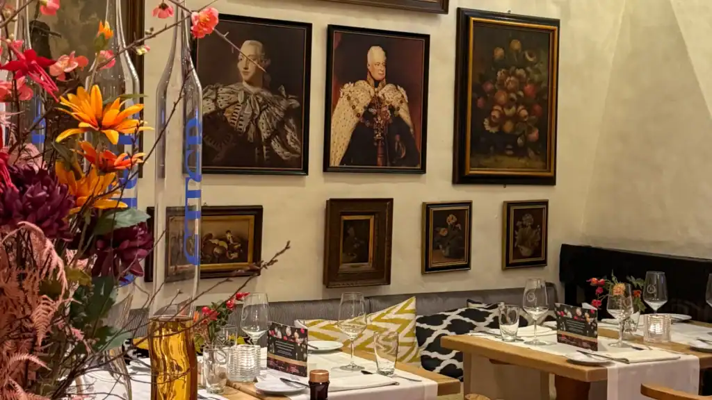 Sammlung von historischen Gemälden an der Wand hinter gedeckten Restauranttischen.