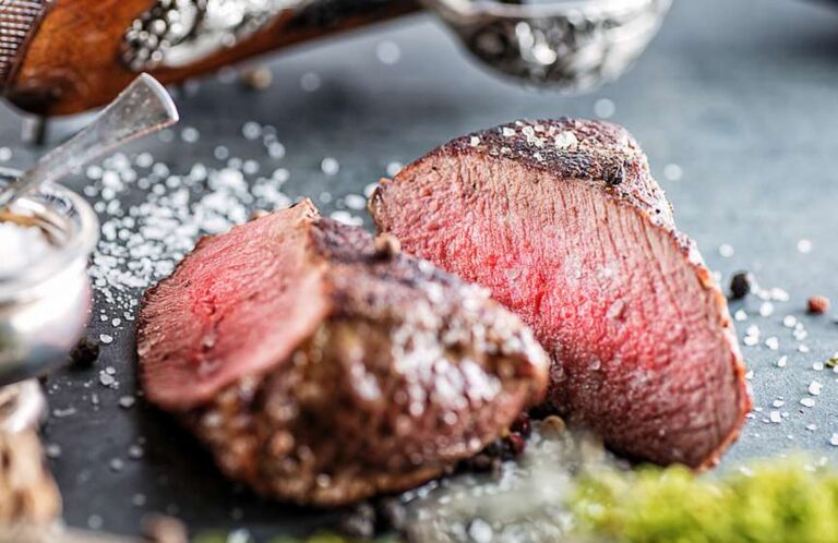 Rosa gebratenes Wildfilet, aufgeschnitten, mit grobem Salz und Pfefferkörnern auf dunkler Schieferplatte